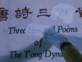 Color image of a white page with Chinese and English printed text on it. A brush with white paint is painting over the word 