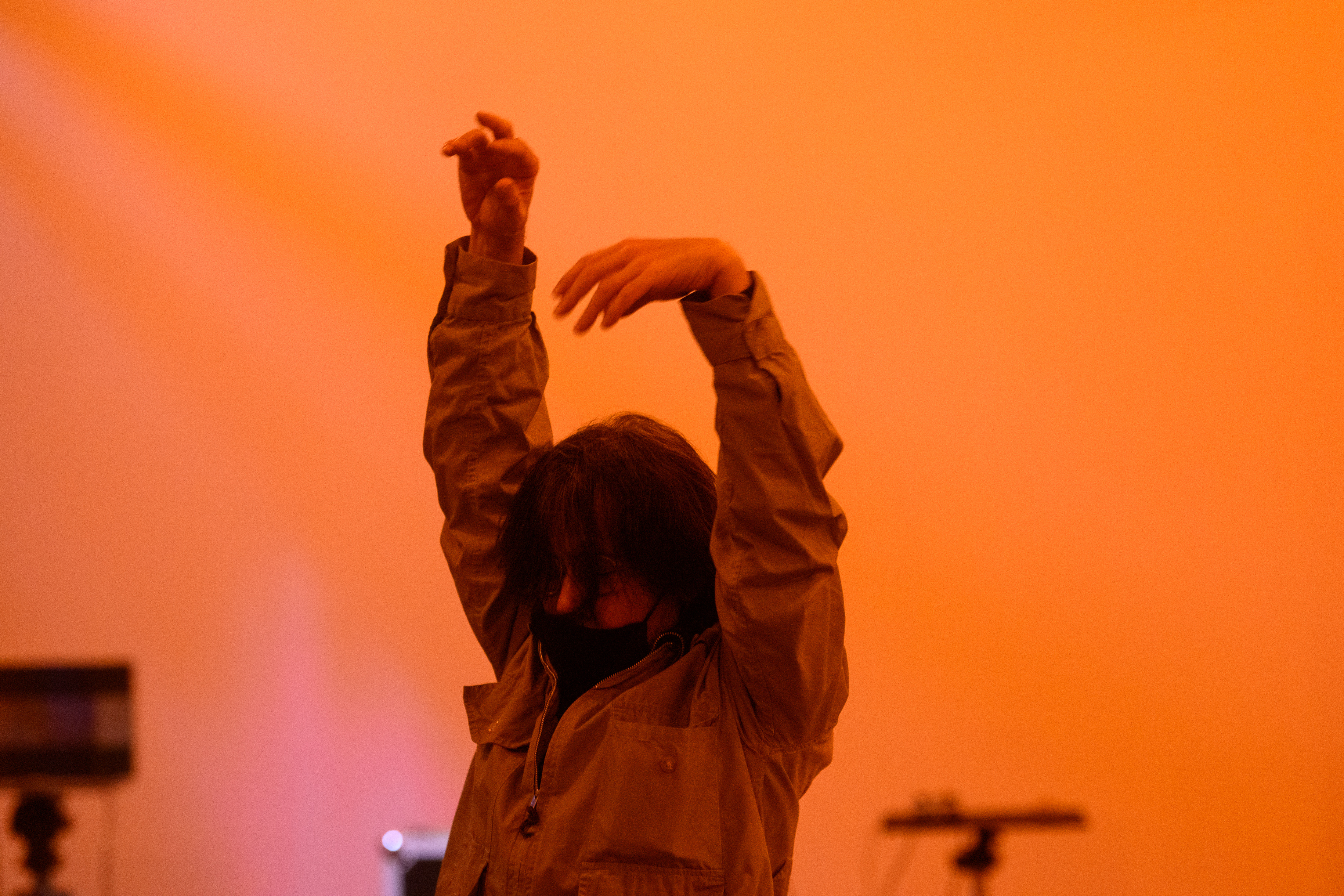 A color photograph of a figure with raised arms in an orange-lit space.