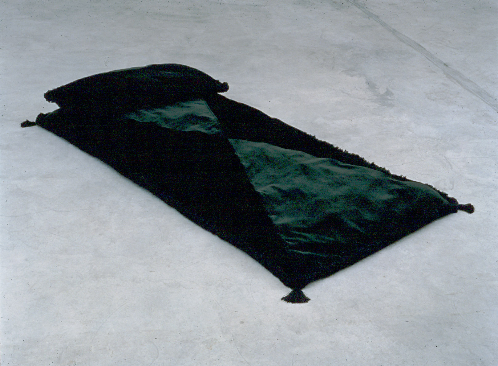 The image shows a rectangular bed-like cushion with a black pillow that lays diagonally across the image patterned with two green and two black triangles of fabric.