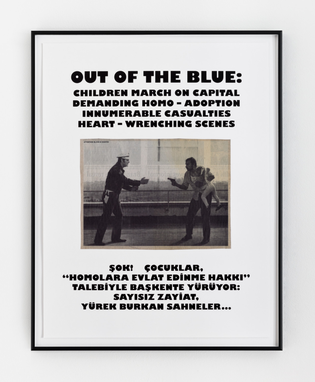 A framed image with black text, white background, and a black & white photo in the center hangs on a wall. The photo depicts a cop on the left who reaches towards a man holding a gun and a young child on the right. Above the photo it says, "Out of the blue: / Children march on capital / demanding homo-adoption / innumerable casualties / heart-wrenching scenes." Beneath the photo, the text repeats but in Turkish.