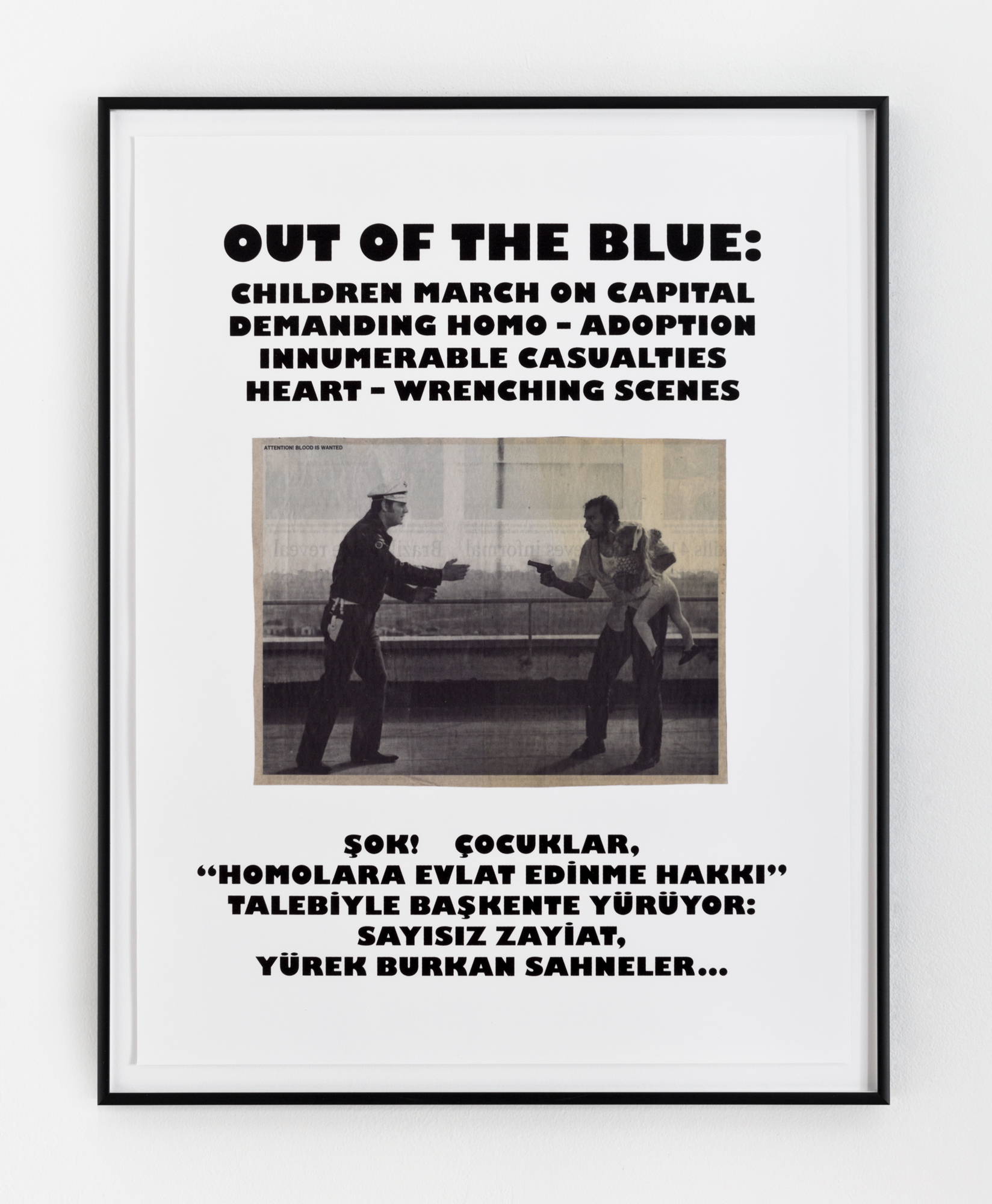 A framed image with black text, white background, and a black & white photo in the center hangs on a wall. The photo depicts a cop on the left who reaches towards a man holding a gun and a young child on the right. Above the photo it says, 