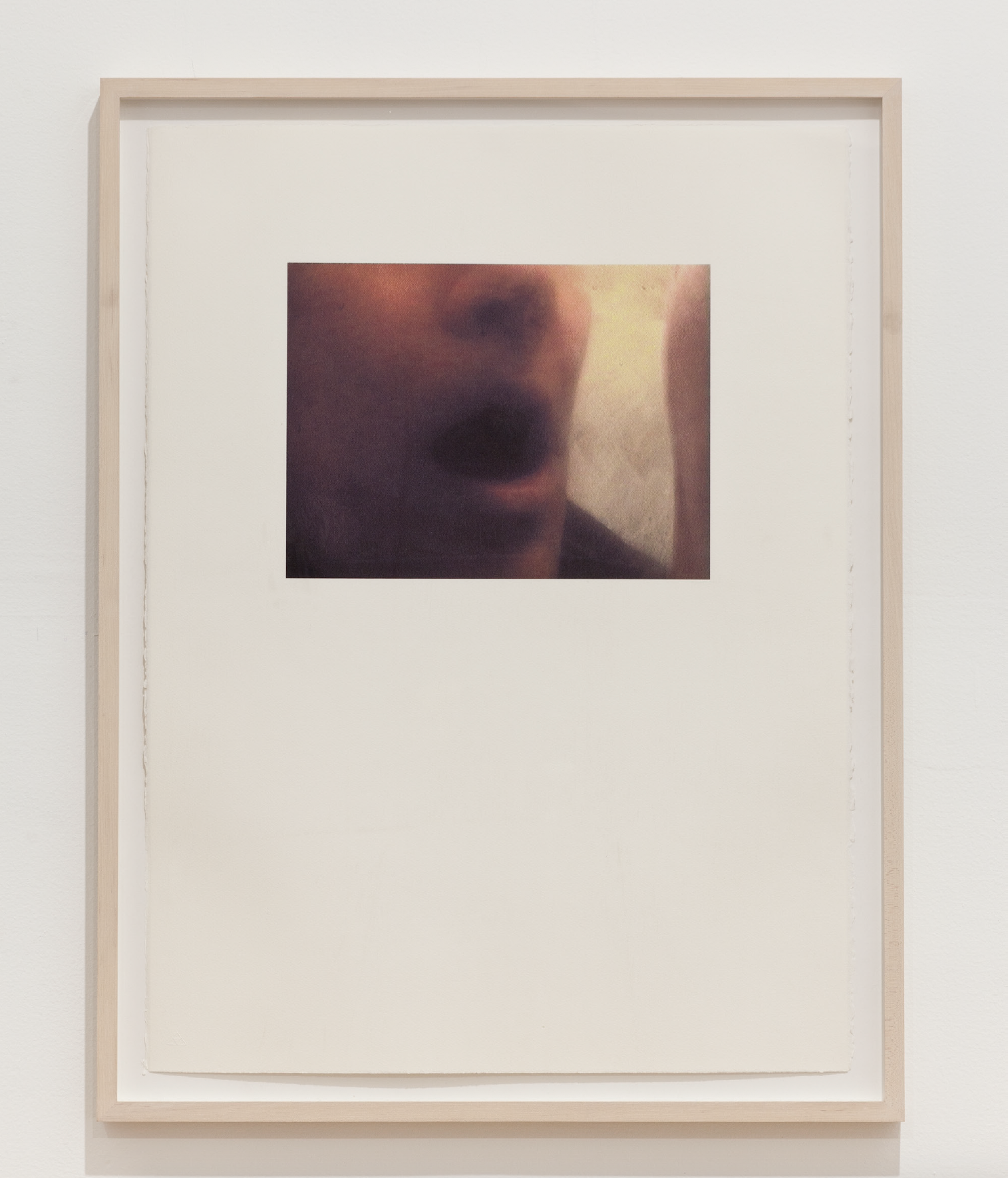A photograph with a wood frame hangs on a wall. The photo sits on a white background, centered in the top half of the page. The photo shows a person's nose and mouth, with mouth agape.