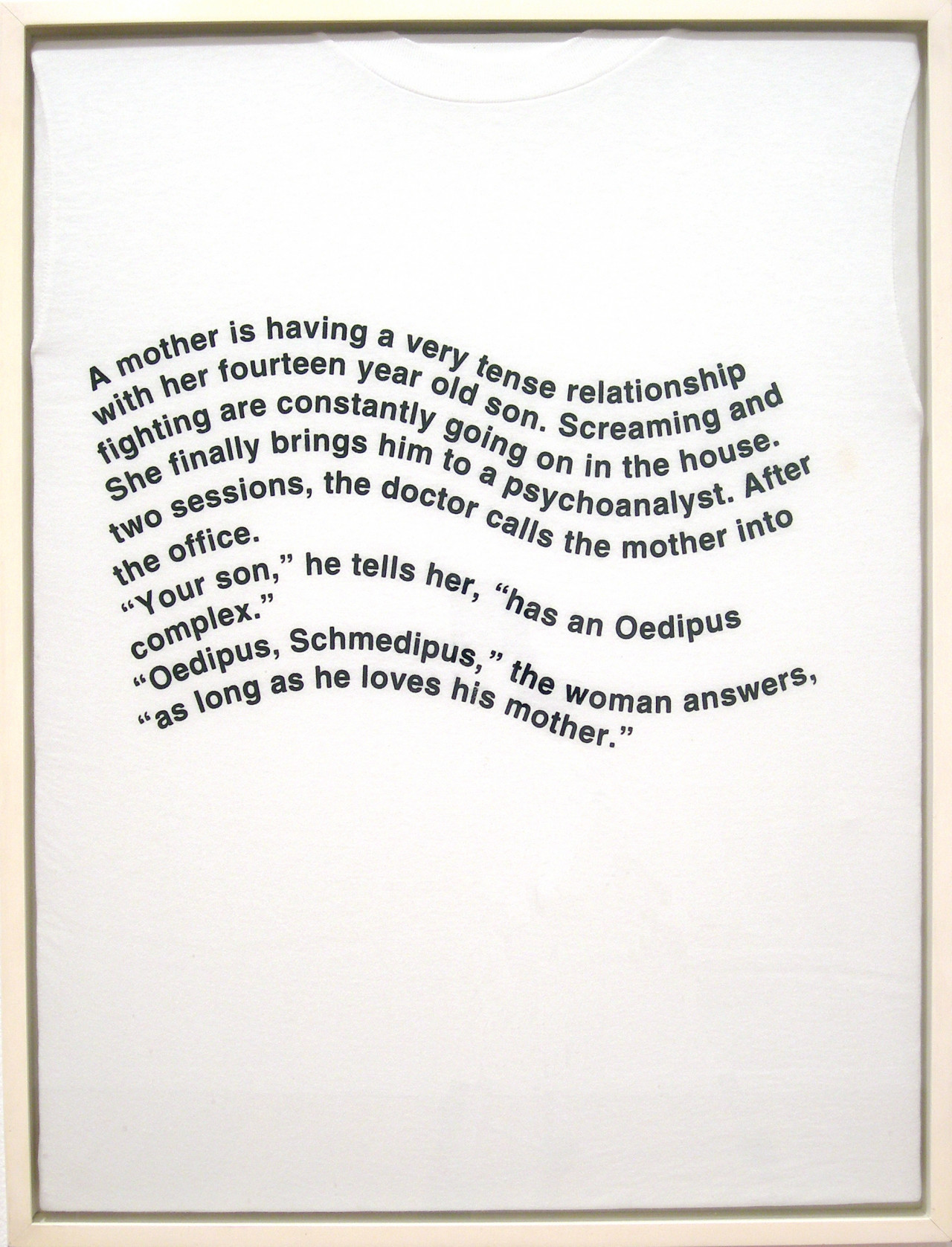 The image shows a white t-shirt in a frame with text printed on top in a wavy text that says, "A mother is having a very tense relationship / with her fourteen year old son. Screaming and / fighting are constantly going on in the house. / She finally brings him to a psychoanalyst. After / two sessions, the doctor calls the mother into / the office. / "Your son," he tells her, "has an Oedipus / complex." / "Oedipus, Schmedipus," the woman answers. / "as long as he loves his mother."