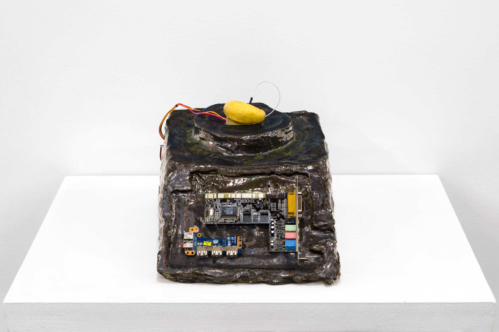 A brown object with a processing chip imbedded in its front sits on a white base. On top of the object, a small potato sits with a wire attached.