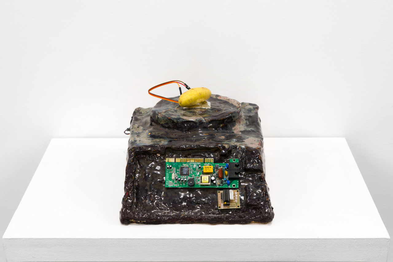 A brown object with a processing chip imbedded in its front sits on a white base. On top of the object, a small potato sits with two wires attached.