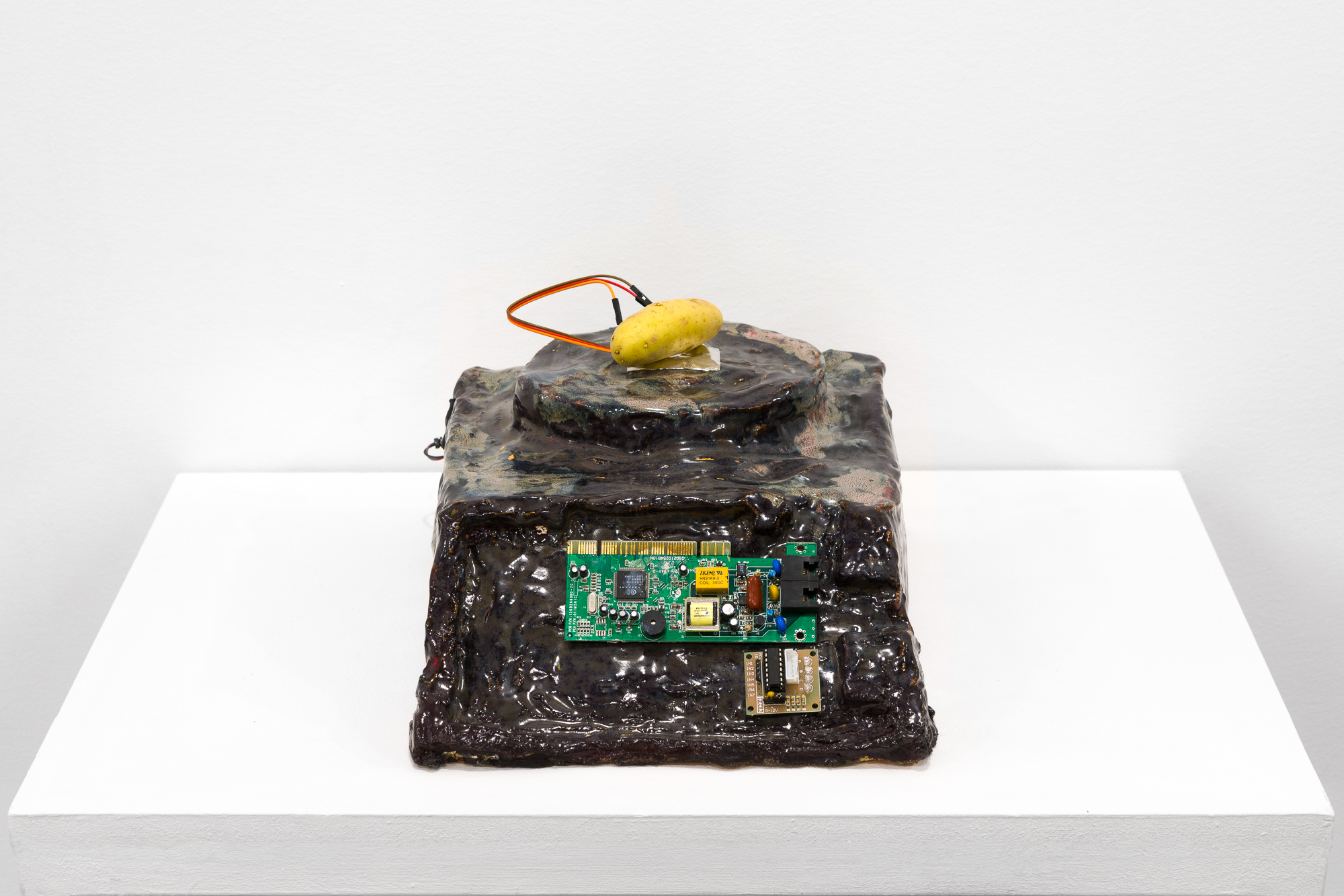 A brown object with a processing chip imbedded in its front sits on a white base. On top of the object, a small potato sits with two wires attached.