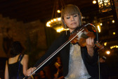 A close-up photo of a violinist performing in front of several people and a chandelier.
