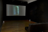 A dimly lit room with a leather black couch facing a projection screen.