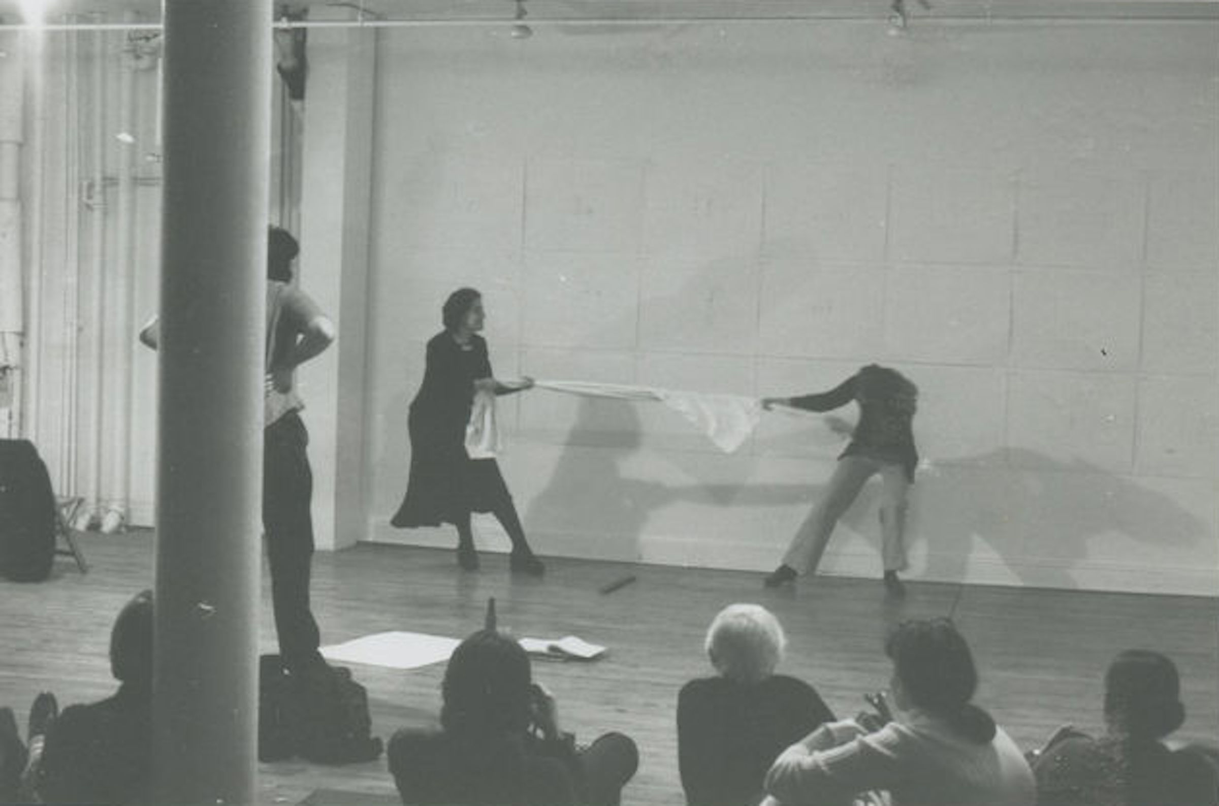 A black and white image of a performance by two individuals tugging on opposite ends of fabric.