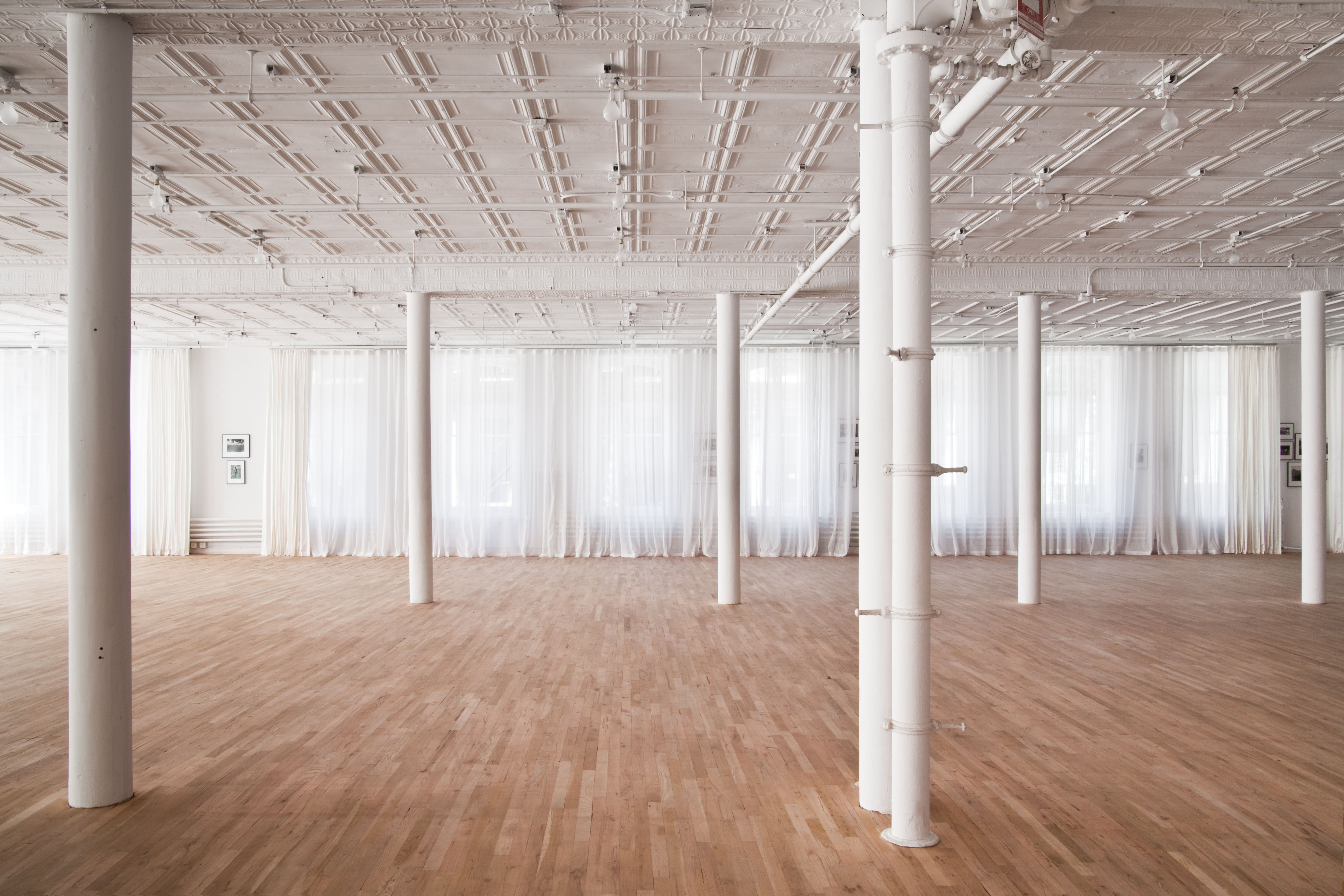 An expansive space with a grid of white columns, sheer curtains cover windows lining the back wall.