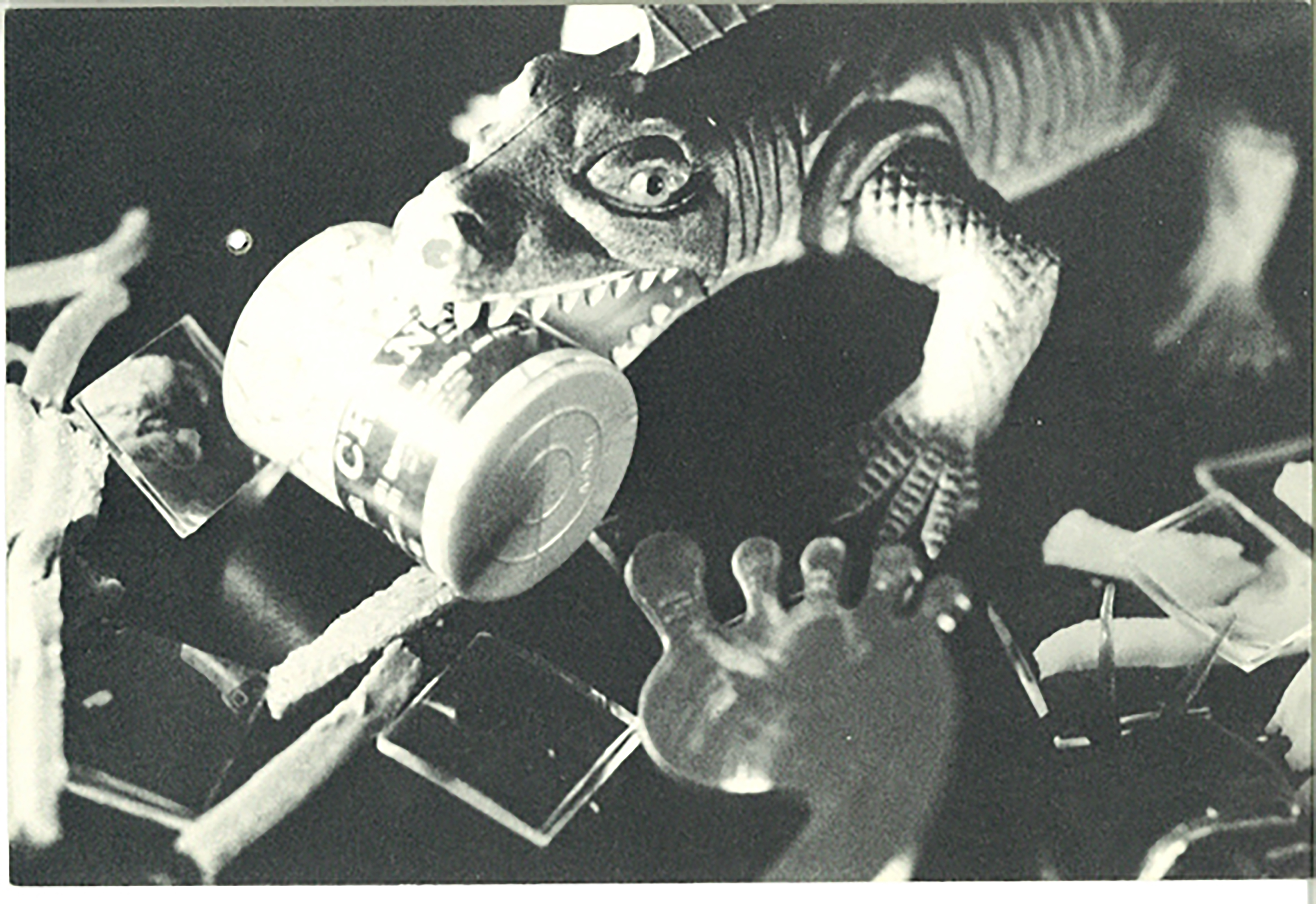 A black and white image of a toy alligator holding a medicine bottle, surrounded by miscellaneous objects.