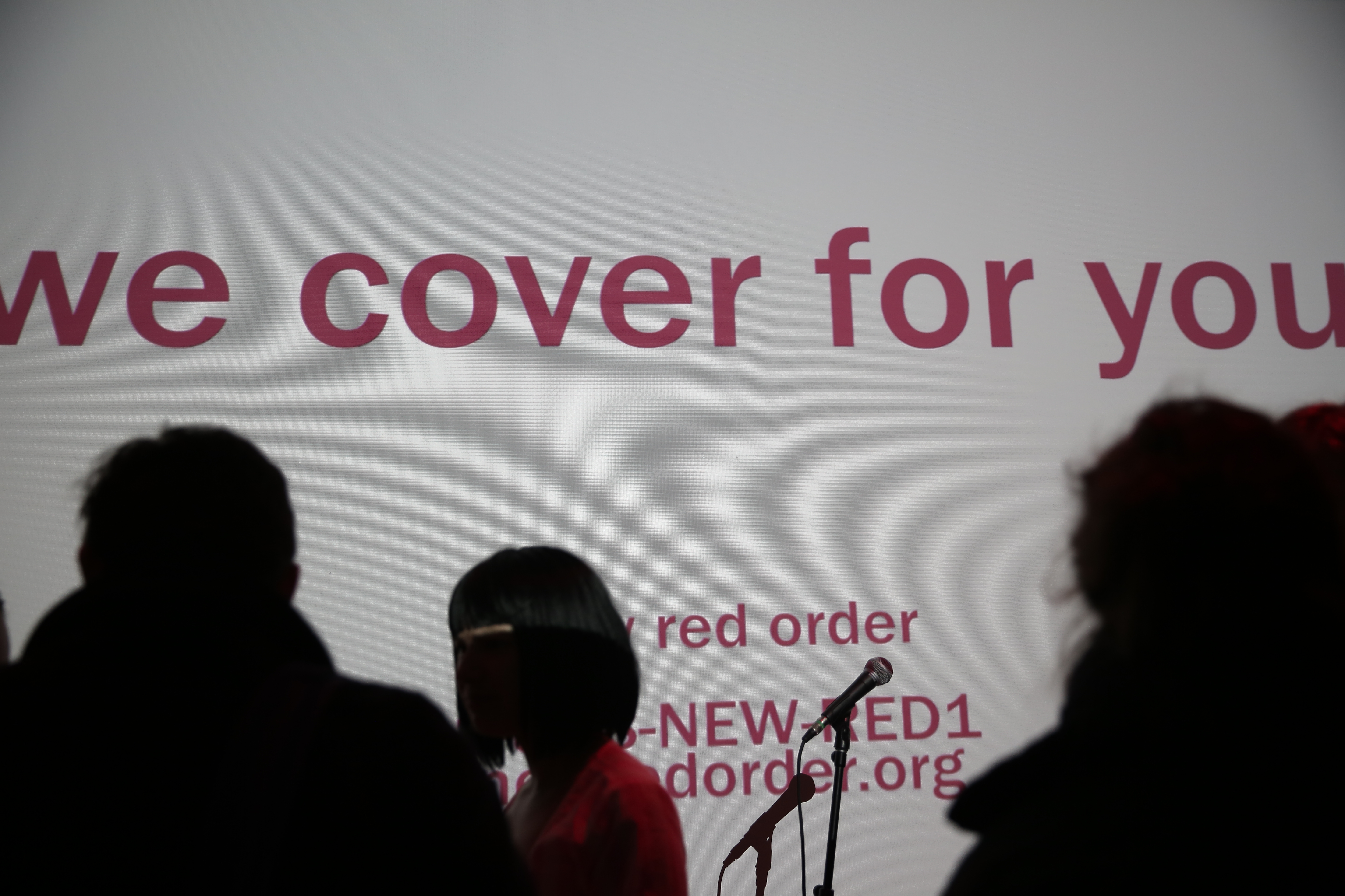 Figures wearing partial face coverings stand in front of a projection that reads: 