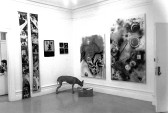 A black and white photograph of an exhibition space with multiple art works.