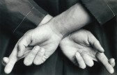 An close up black and white image of an individual with their fingers crossed behind their back.